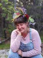 Mumbleweeds' artist Stevie Driscoll, sitting happily on her land, wearing overalls and flowers in her hair